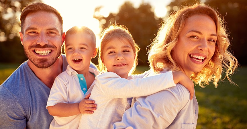 Young family woman, man and two children smiling in the sun